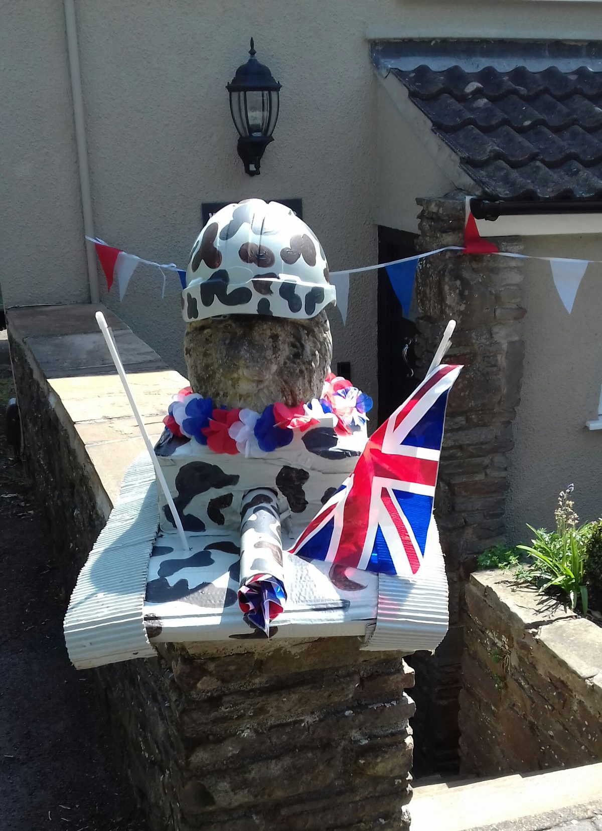 A lion gate post ornament is seated in a tank with a Union Jack for V.E. day